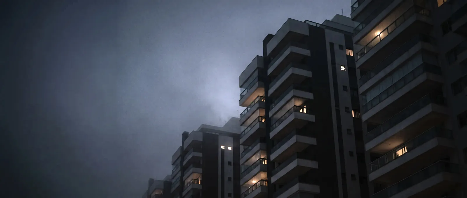 Edifícios residenciais vistos de baixo ao anoitecer, com algumas janelas acesas